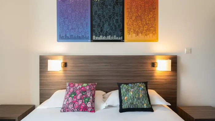 A bedroom with a bed, pillows, and a wall painting at Appart’Hôtel Hévéa.