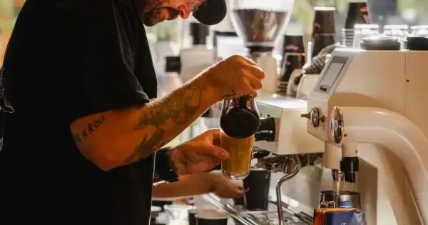 Man in black shirt and hat brewing coffee behind kitchen counter