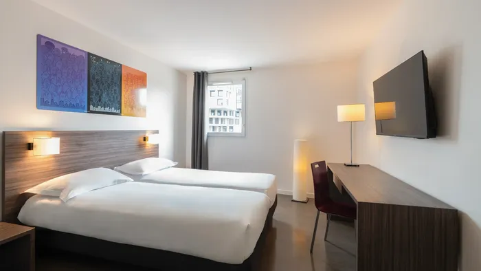 Twin beds, a desk, and a television in a modern hotel room at Appart’Hôtel Hévéa.