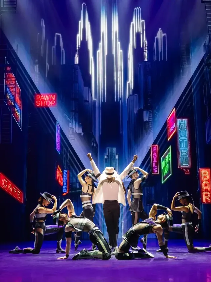 Performers on stage under neon signs for MJ the Musical.