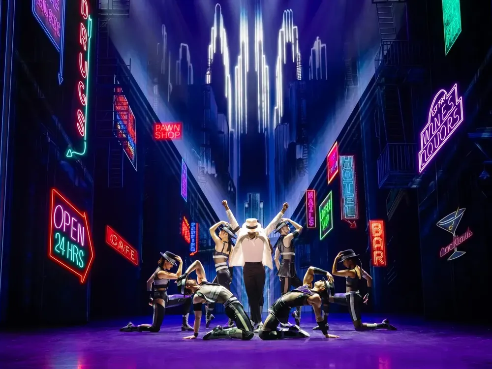 Performers on stage under neon signs for MJ the Musical.