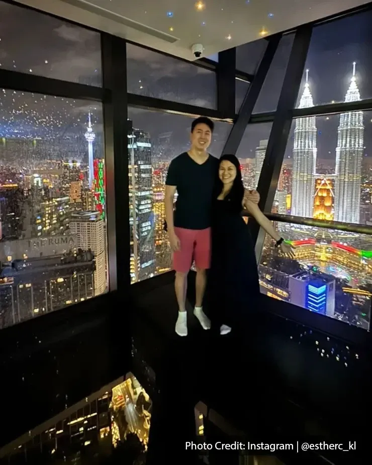 A couple smiles for a photo in front of the Petronas Towers, capturing a romantic moment during their staycation.
