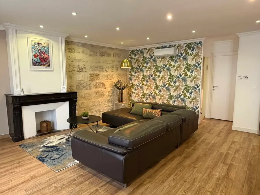 Cozy living area with a fireplace, tropical wall decor, and a sectional sofa at Le Grand Hôtel Molière, Pézenas.