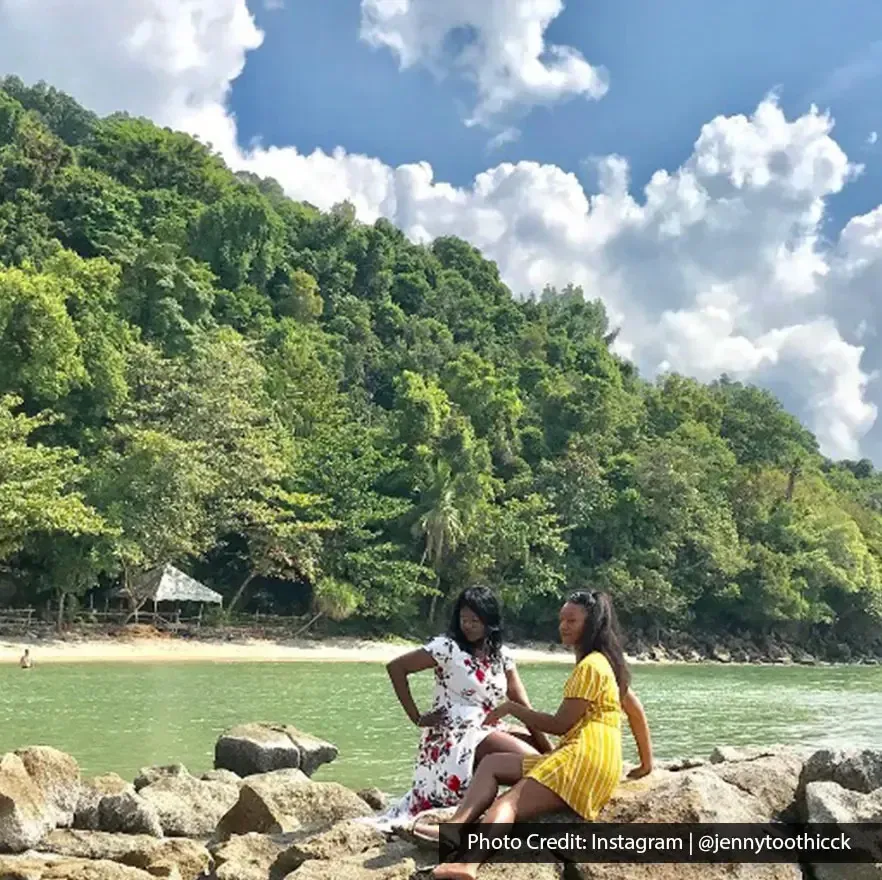 Two women relaxing on coastal rocks with scenic backdrop at Tanjung Asam