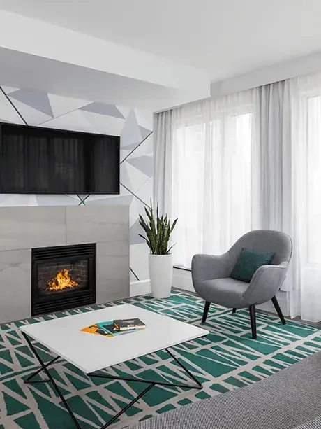 Modern living room featuring a gray armchair with geometric rug, and a cozy fireplace at Warwick New York 