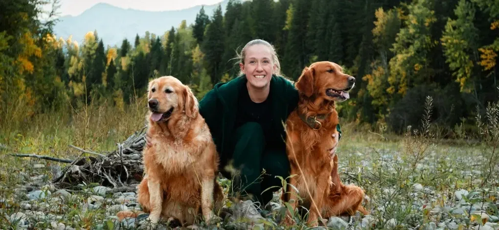Person poses with their dogs in an off-leash dog park in Canmore.