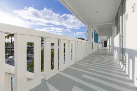 Second-floor exterior corridor at The Vagabond Hotel Miami with white railings, turquoise accents, and long afternoon shadows