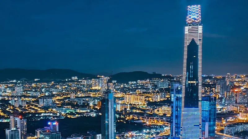 A nighttime cityscape with multiple illuminated skyscrapers and a prominent tall building with blue lights.