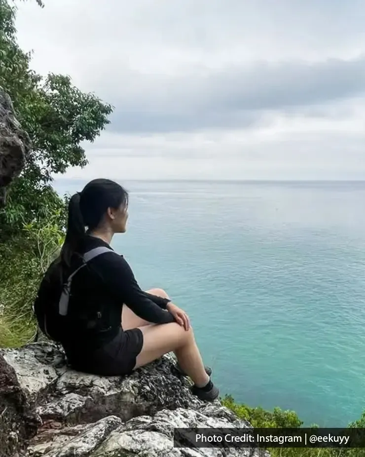Seorang wanita duduk di atas batu tepi bukit sambil melihat ke laut tenang - Lexis Hibiscus Port Dickson