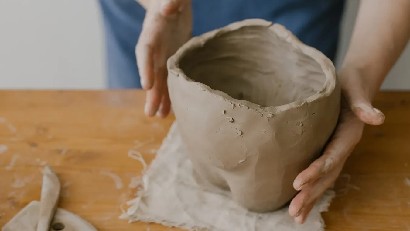 Person's hands holding a raw clay bowl on a wooden table at Good Times DIY Pottery & Tufting Studio.