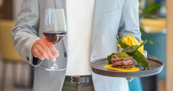 Man holds a plate of food and a glass of red wine at Forester Bar & Grill