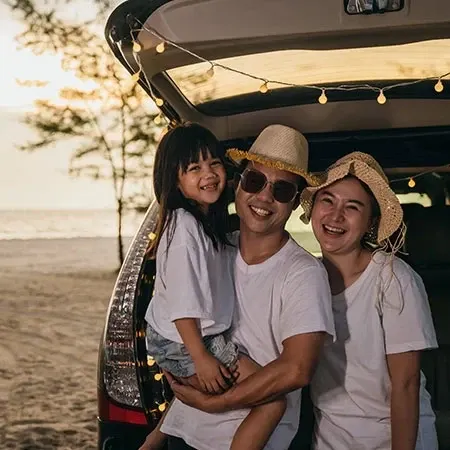 Two adults and child smiling by open car trunk