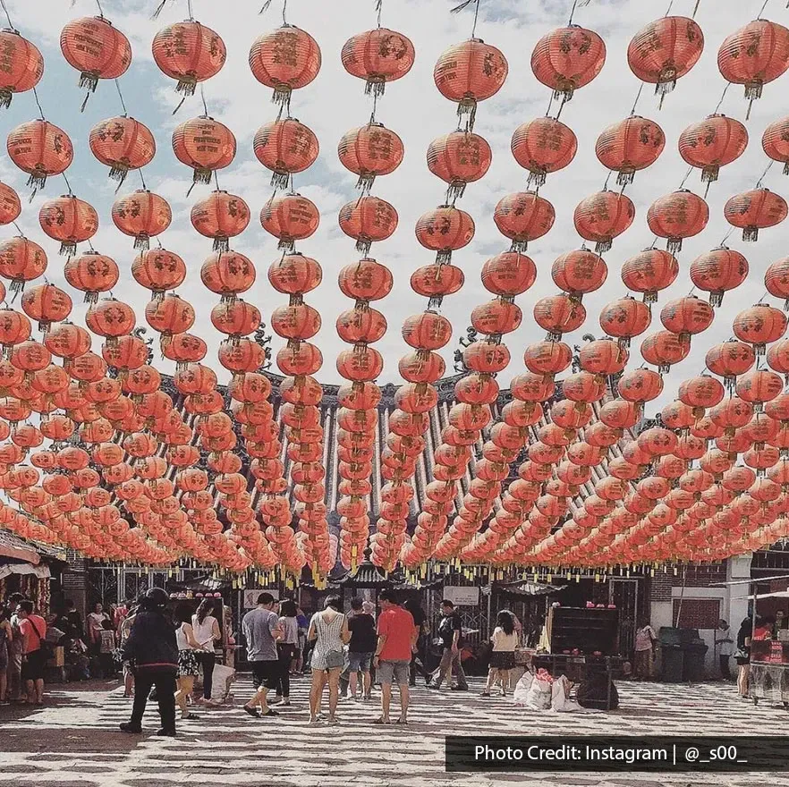 People exploring Goddess of Mercy Temple with rows of red lanterns overhead in George Town Penang.
