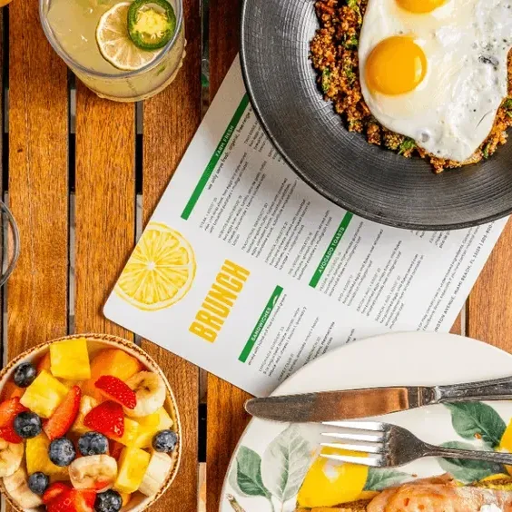 Plate of eggs, fruit bowl, and drinks on a wooden table with a menu card labeled 