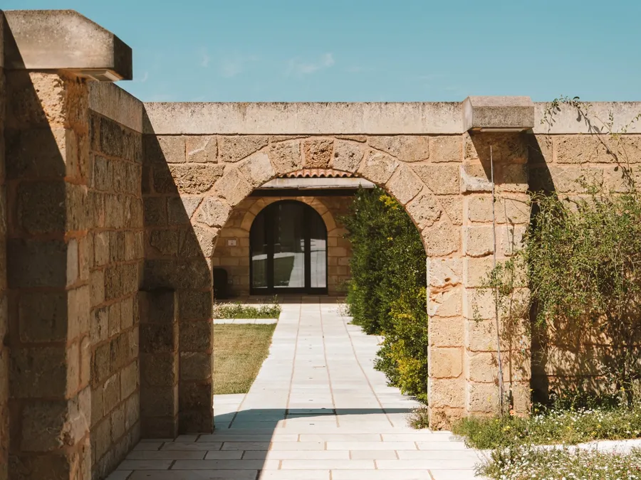 Allée pavée bordée de murs en pierre et d'arbustes menant à une arche à Masseria Stali