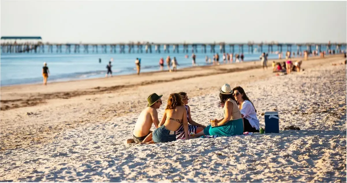 A group of bathers sit on the sand at Henley Beach, Adelaide.