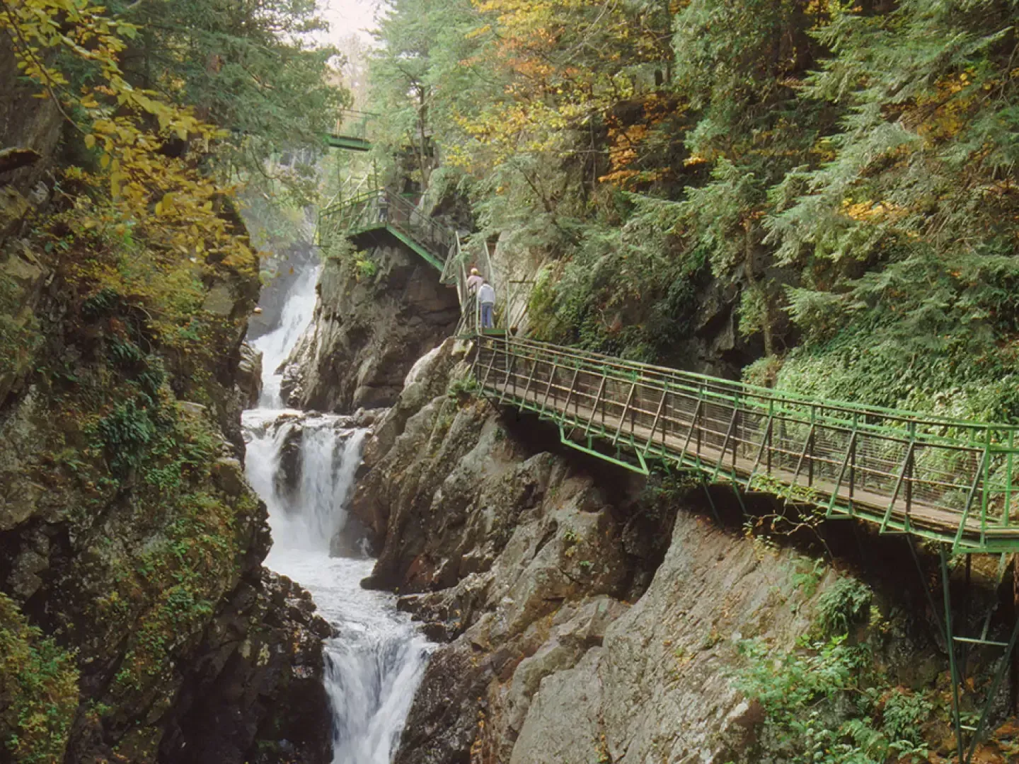 Hikers traverse a scenic bridge path overlooking rushing waterfalls and rock gorges near Lake Placid Club Grandview