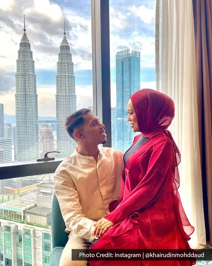 A man and woman dressed in red perched on a window ledge with Kuala Lumpur skyline in background.
