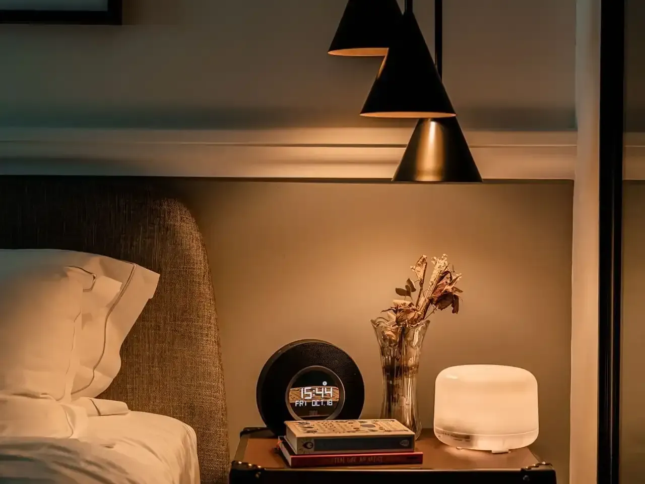 Warm bedroom with nightstand, clock, books and vase of dried flowers at Grand Park City Hall