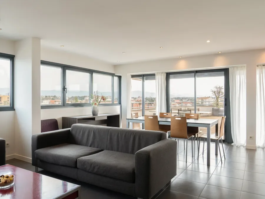Living area with a couch, dining table, and kitchen view in a two-bedroom apartment at Appart’Hôtel Hévéa in Valence.