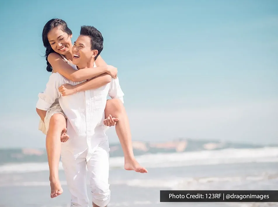 Romantic couple enjoying piggyback ride together by the ocean shore.