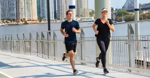 A smiling woman and man jogging alongside each other on the Brisbane Bridge