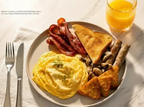 Breakfast plate with scrambled eggs, bacon, toast, sausage links, hash browns, and orange juice on marble surface