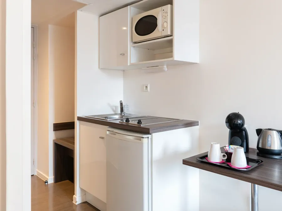 Modern kitchen with microwave, sink, coffee maker, and kettle in Triple Studio at Appart’Hôtel Hévéa, Valence.