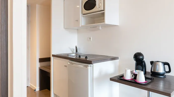 A compact kitchen area with white appliances and modern fixtures in a hotel room at Appart’Hôtel Hévéa.