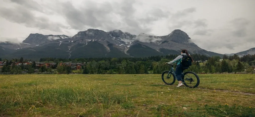 A person on a bike trail stops to stare at the mountains on a flat biking trail in Canmore.