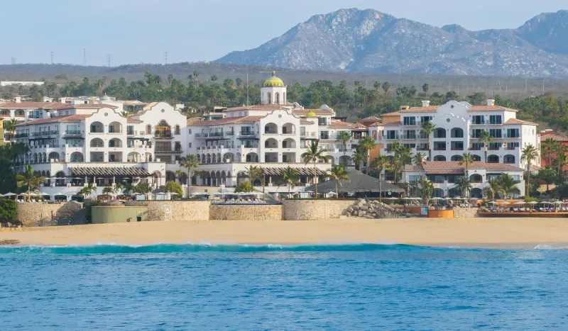 Hotel Hacienda del Mar Los Cabos with a beach in front, surrounded by mountains and palm trees.
