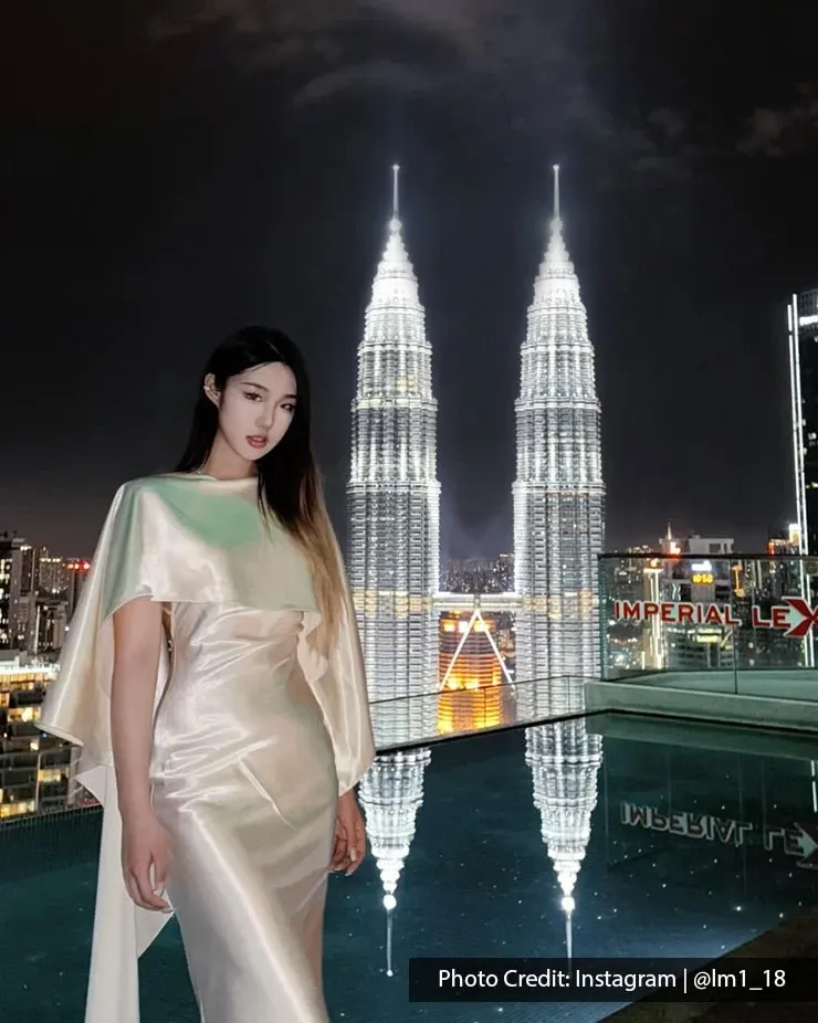 A woman poses in beautiful dress by the pool with the iconic Petronas Twin Towers brightly lit at night.