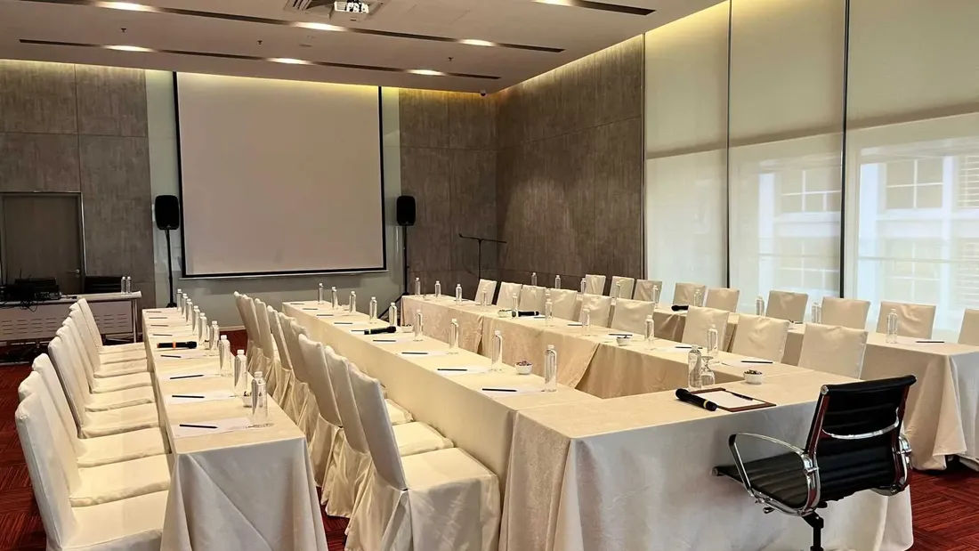 U-shaped table arrangement and white fabric chairs facing a projector screen in a meeting room at Sunway Velocity Hotel