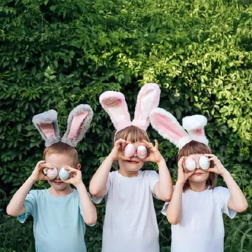 Three children wearing bunny ears and holding Easter eggs over their eyes at Bensaude Hotels
