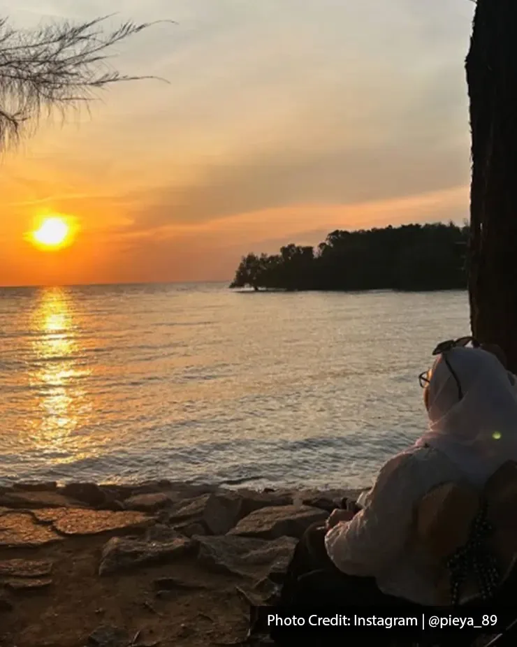 Seorang wanita duduk menghadap laut menikmati pemandangan matahari terbenam indah di tepi pantai - Lexis Hibiscus Port Dickson