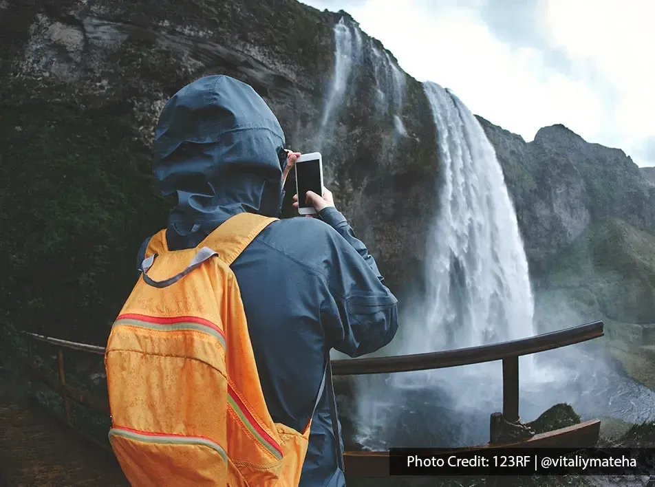 Explorer in rain gear photographing waterfall at top adventure activities location - Lexis Hibiscus Port Dickson