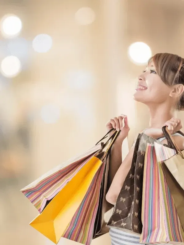 Une femme rayonnante, portant plusieurs sacs de courses colorés, passe devant l'intérieur flou d'une boutique près de Warwick Hotels & Resorts