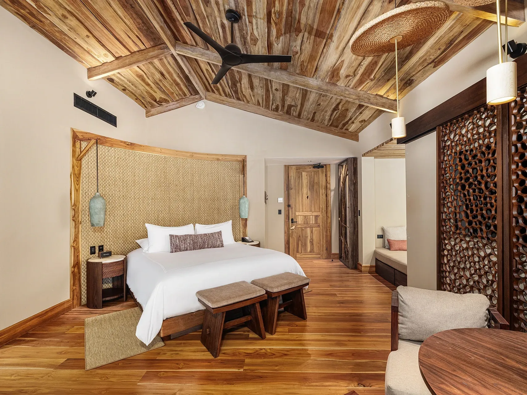 Bed with woven headboard, stools at foot, and hanging lights over table in Deluxe River Bliss at Santa Lucia Jungle Hacienda