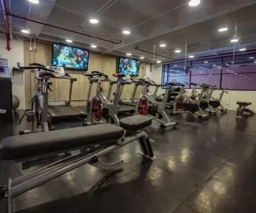 Modern fitness gym with exercise bikes and treadmills beneath glowing mounted televisions at Unika Hotels