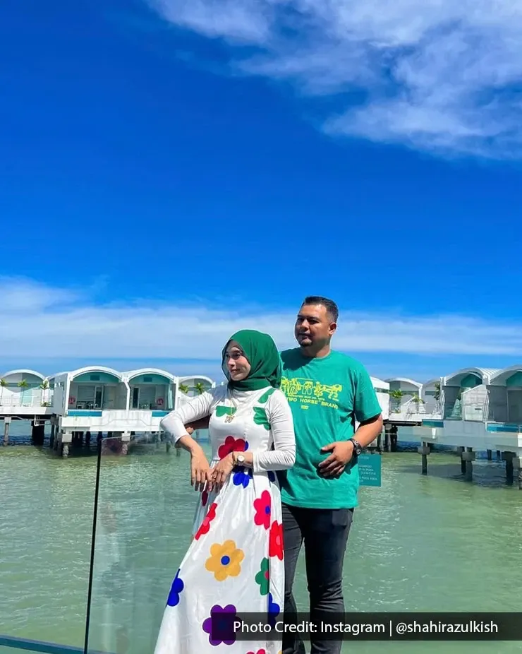 Couple standing together by the water with overwater villas.
